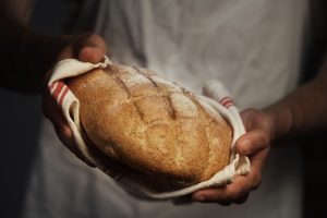 A baker holding fresh sourdough in a white towel