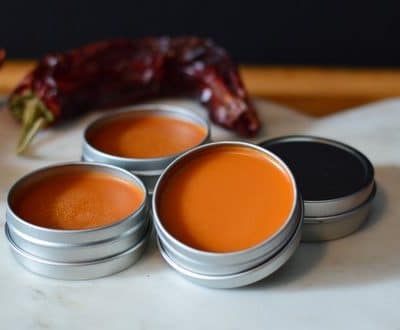 Tins of cayenne salve by a red cayenne pepper