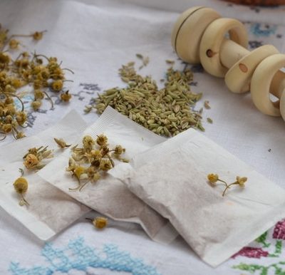 A baby rattle and tea bags of homemade gripe water with herbs lying beside them