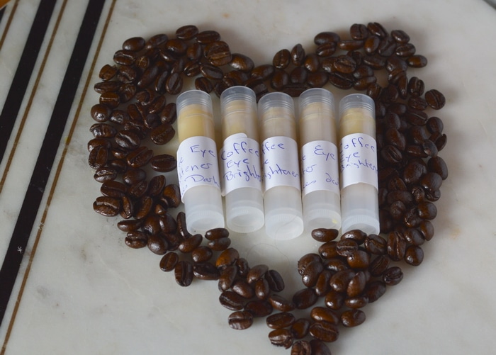 Tubes of homemade eye cream surrounded by coffee beans in the shape of a heart