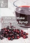 Fresh elderberries sitting on board by glass of elderberry syrup