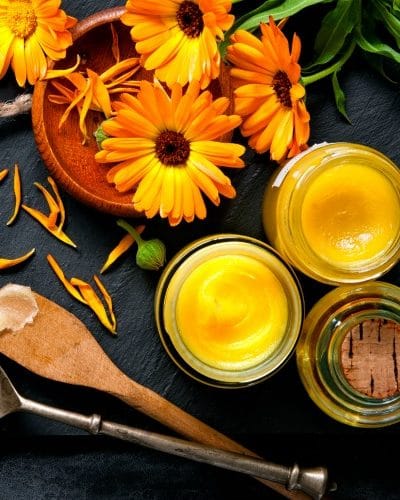 Fresh calendula flowers by jars of yellow salve